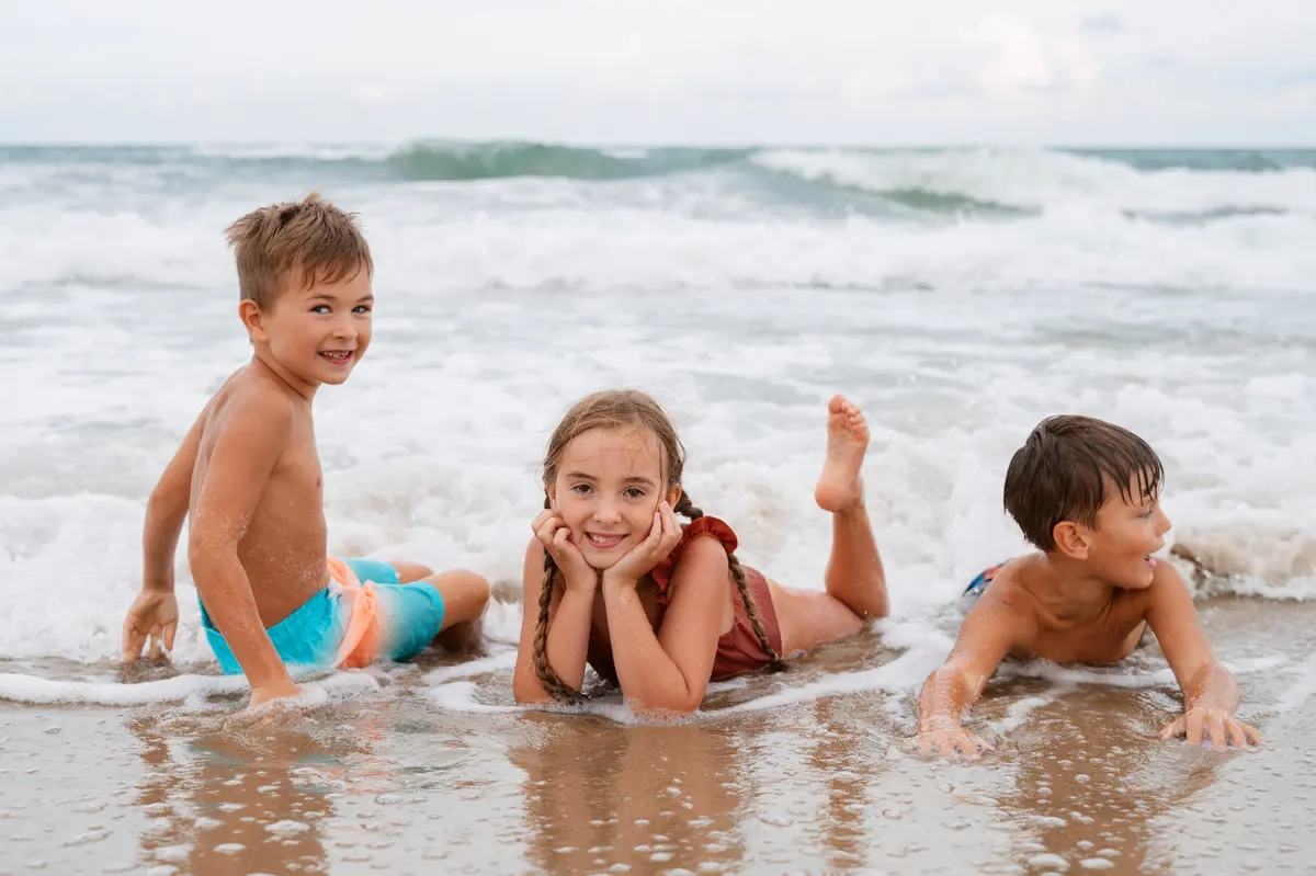 Three children lying in the shallows at the water's edge, smiling
