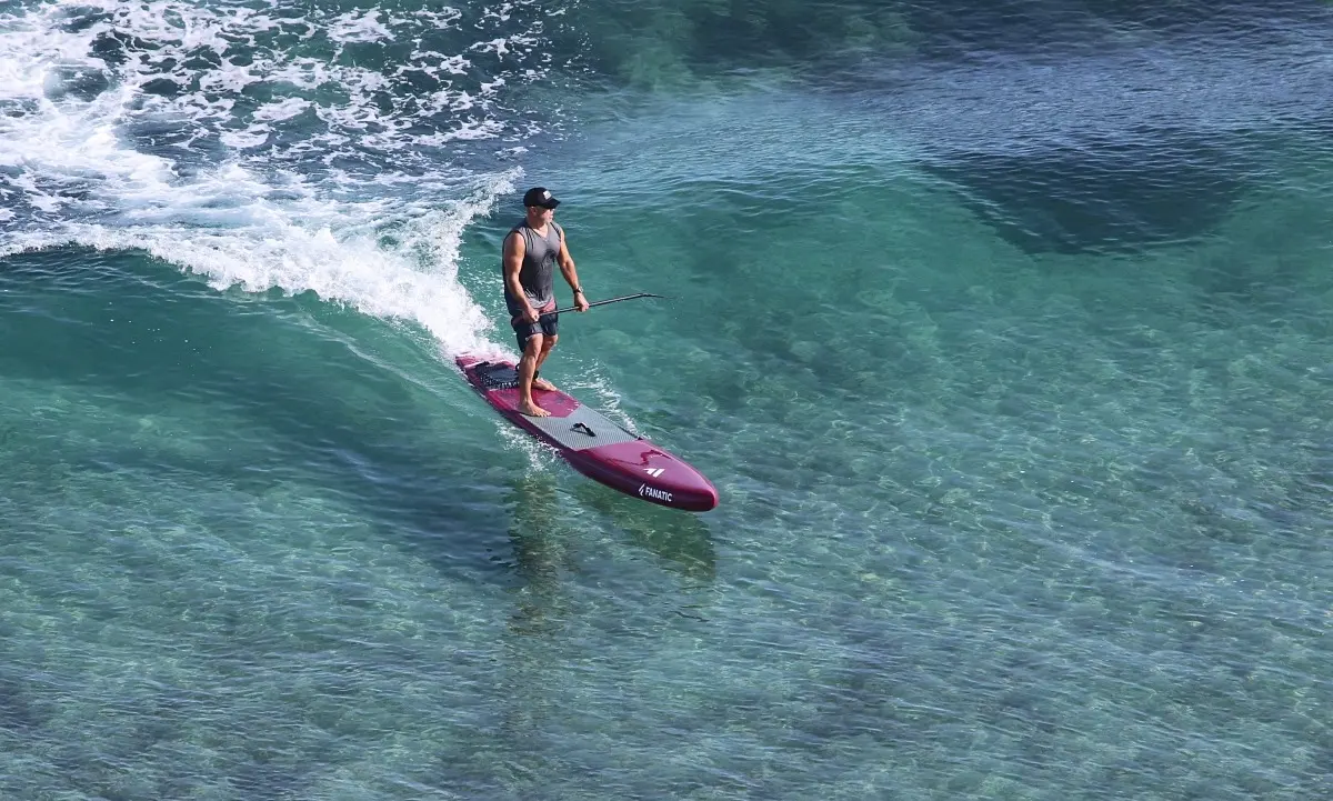 Paddle boarder riding a small wave in clear turquoise water